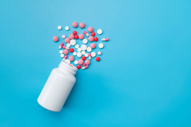 istock Multi-colored tablets, pills, capsules, vitamins spilling out of white plastic container on blue background, flat lay top view. Concept of medicine, health care, pharmaceuticals 2164633558