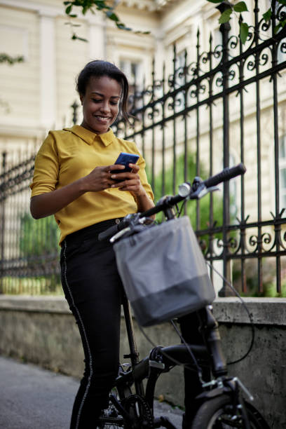 istock Smiling young woman with bicycle using mobile phone in city park. 2164640614