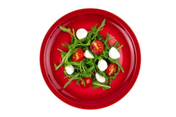 istock Mediterranean salad with arugula tomatoes and mozzarella on a red plate top view, isolated on white 2164642728