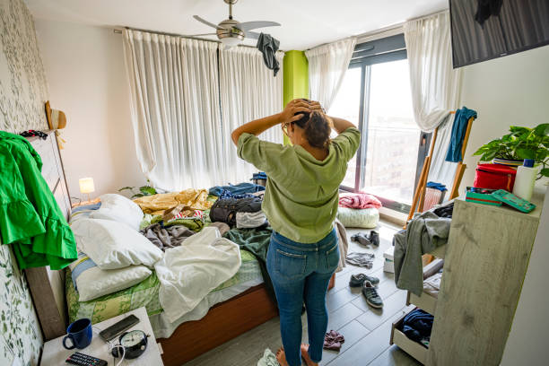 Upset woman head in hands contempling her messy bedroom