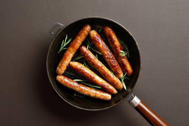 istock Delicious thin sausages in frying pan on brown background 2164653374