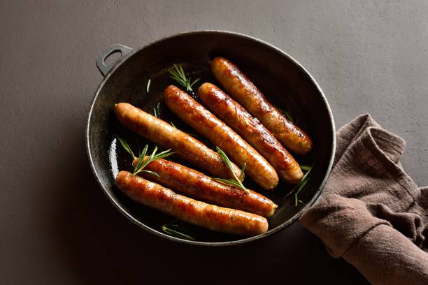 istock Delicious thin sausages in frying pan on dark background 2164653406