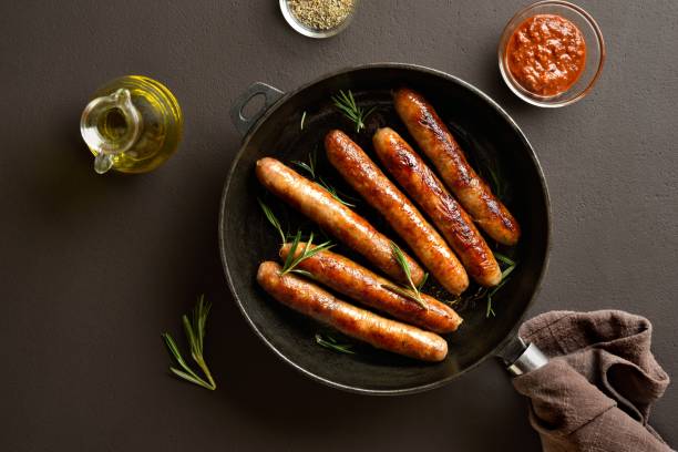 istock Delicious thin sausages in frying pan on brown background 2164653931
