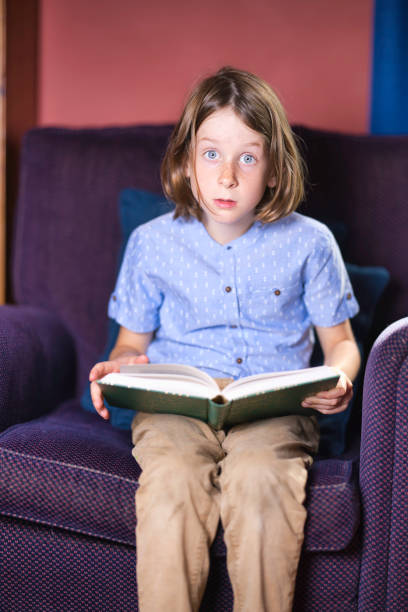 Blue-eyed boy with long, straight hair reading a book.
