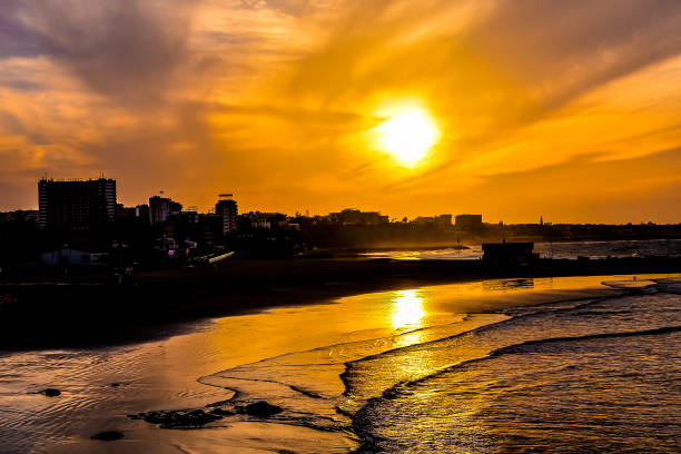 A beautiful sunset over a beach with a city in the background A beautiful sunset over a beach with a city in the background. The sky is filled with clouds and the sun is setting, creating a warm and peaceful atmosphere sunset agadir marocco stock pictures, royalty-free photos & images