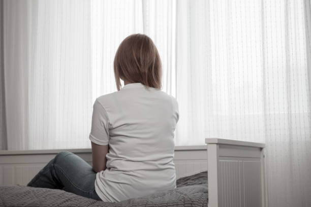 istock Depressed woman: sitting, hugging her knees, head down, face hidden by hair, expression of despair and sadness 2164662484