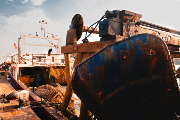 A fishing boat docked at the port of Barcelona with fishing equipment on deck and a clear sky in the background.