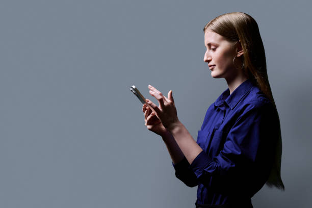 istock College student girl using smartphone, profile view, gray background 2164665653