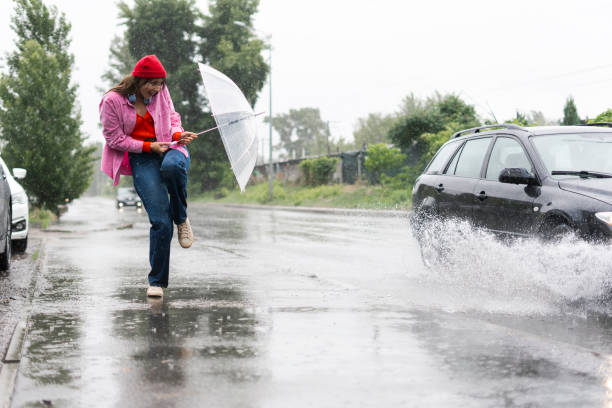 Car splashing on pedestrian outdoors. Scared woman hiding from spray with transparent umbrella. Bad weather concept