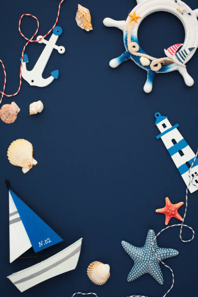 istock Nautical flat lay vertical composition with a ship’s wheel, lighthouse, anchor, starfish, seashells, and a sailboat model on navy blue background. 2164703452