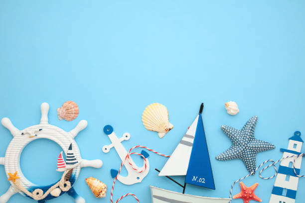 istock Nautical themed decor on a blue background featuring a sea ​​wheel, seashells, starfish, anchor, lighthouse and sailboat. Perfect for summer and beach vacation themes 2164703533