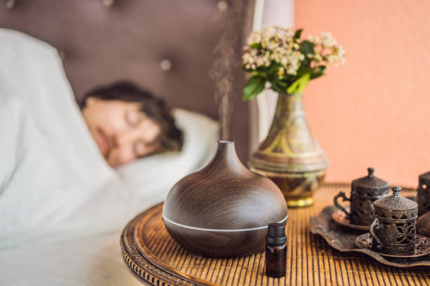 aromatherapy concept. wooden electric ultrasonic essential oil aroma diffuser and humidifier. ultrasonic aroma diffuser for home. man resting at home - diffuseur huiles essentielles photos et images de collection