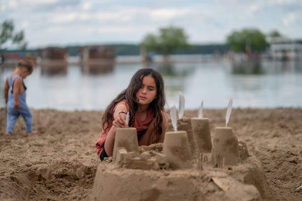 Two young siblings pay together in the sand during a family camping trip.  They are both dressed comfortably and are focused on building a sandcastle together.