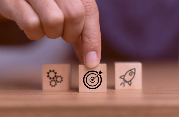 istock Hand touching and push target board which printing on wooden cube block on mechanical gear and rocket icon set up business objective target goal concept. Targeting the business concept. 2164726282