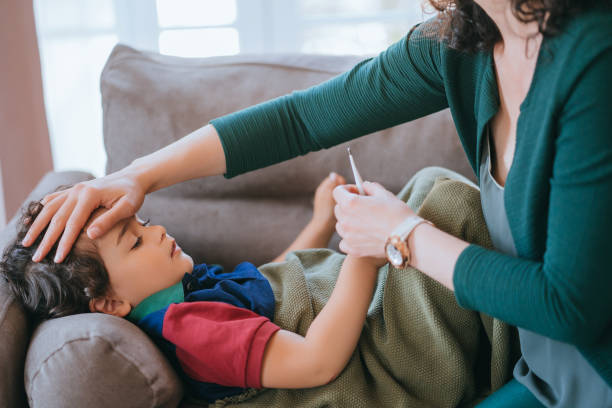 istock mother checking her young son's temperature with a thermometer while he lies on a couch under a blanket, capturing a caring and nurturing moment at home 2164732366