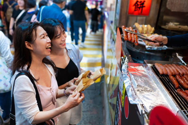 Two Asian women enjoying red bean pancakes while exploring the bustling Jiufen old street in Taipei, Taiwan Two female Asian tourists take a break to savor the delicious red bean pancakes at the bustling Jiufen old street in Taipei, Taiwan. red bean dessert stock pictures, royalty-free photos & images