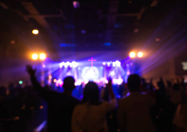 Blurred image of worship concert crowd in front of stage blurred background. Worship includes music and numerous people lifting their hands in praise to God on stage church like a holy light from god stock pictures, royalty-free photos & images