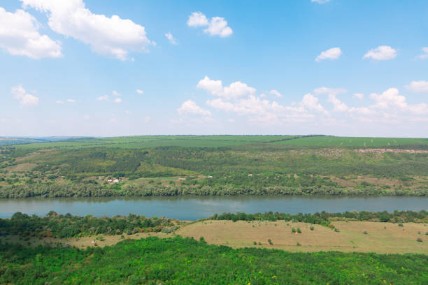 Green landscape with flowing river. Sky is clear and blue, and the trees are lush and green. Riverside scene is peaceful and serene