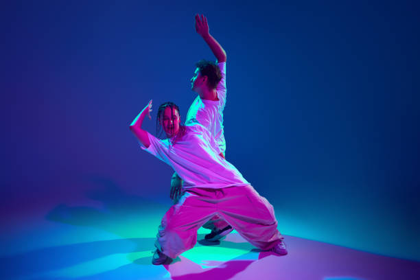 istock Cheerful, talented, positive young man and woman dancing hip-hop, making dynamic performance against purple studio background in neon light 2164746790