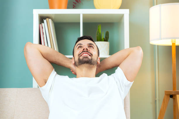 istock Young man smiling at camera as he leans towards the house couch inside. 2164748266