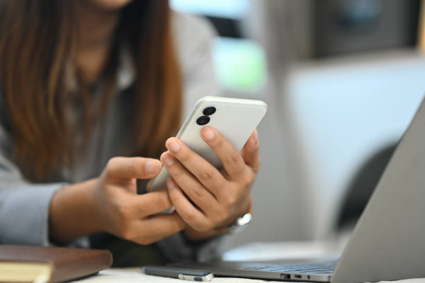 istock Close up woman hands typing massage on mobile phone while using laptop at coffee table 2164749909