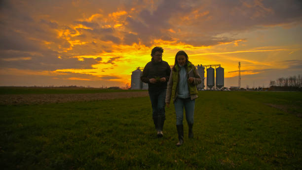 An Agronomist Walks Across a Farm,Discussing Crops with a Dramatic Sky Overhead. Silos Stand in the Background,Highlighting the Rural Setting and Agricultural Focus of the Conversation