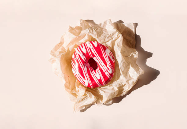 istock Pink glazed doughnut with white drizzle on crumpled parchment paper. 2164778340