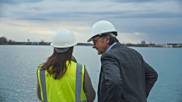 istock Serious Architect Discussing Water Conservation with Female Engineer in Protective Workwear while Standing at Lake Reservoir 2164778523