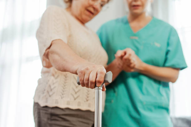 istock Elderly woman using walking stick with nurse standing in background, selective focus on hand 2164778671