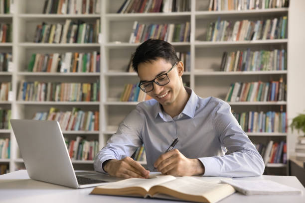 istock Smiling intelligent Indian student guy makes exercise in copybook 2164781291