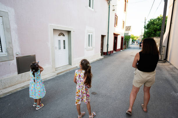 A mother and her two daughters walk along a charming, quiet street on a sunny day. The children appear curious and joyful in Nin, Croatia.