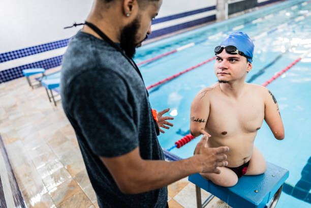 istock Competitive para athlete swimmer with double arm and leg amputations talking with instructor at swimming pool 2164800466
