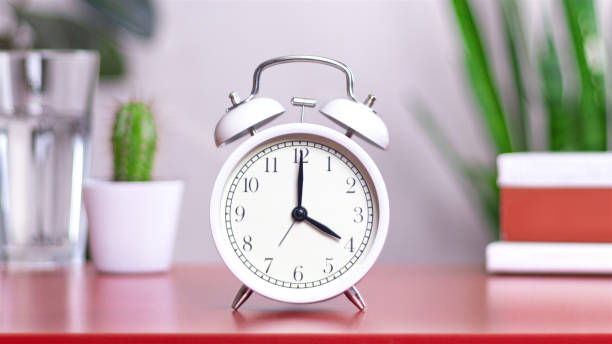 istock Classic white clock on a table. The clock hand points to 4 or 16, close up 2164803719