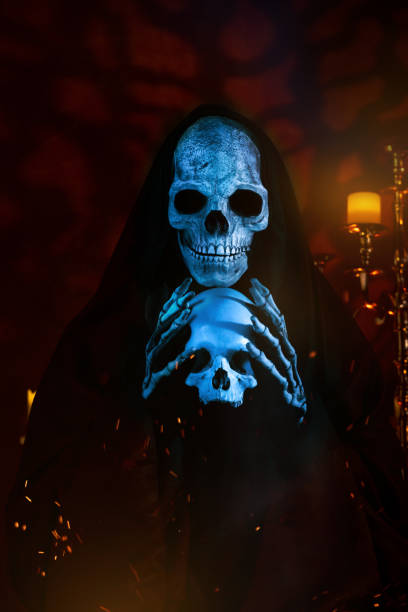 Grim Reaper illuminated by blue light in a dark room, holding a human skull.