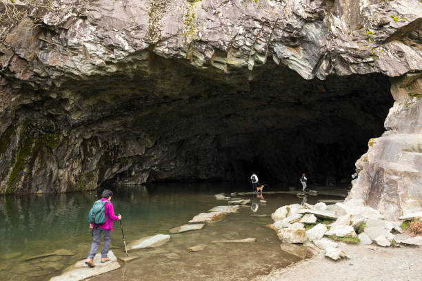 Cumbria, UK - April 21, 2024. Hikers walk on stepping stones at the entrance to Rydal Cave near Ambleside, Lake District, UK