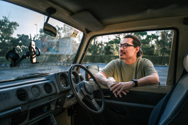 Asian chinese man leaning on SUV car looking away weekend morning with backlit sunlight