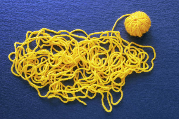 Tangled yellow threads and attempt to wind threads into ball.  Black background, flat lay, copy space