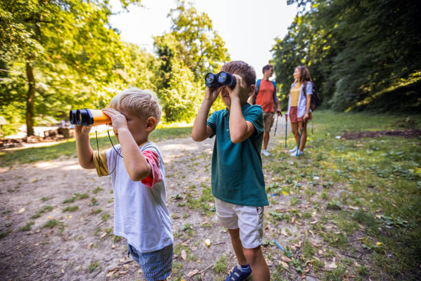 Two little brothers looking through binoculars. Exploring the nature in the park.
