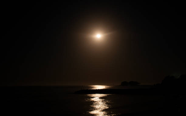 full moon in reflection in the sea in dark night warm light horizon