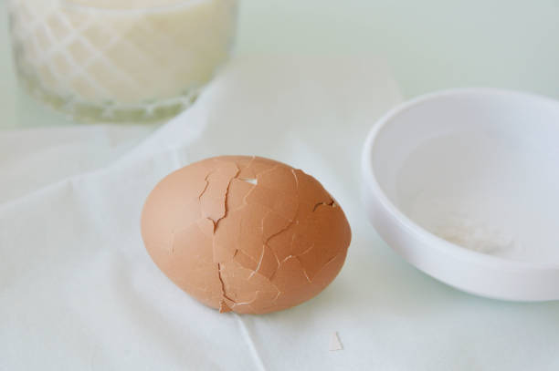 istock Cracking shell of a boiled egg in a white background with a glass of milk. 2164826565