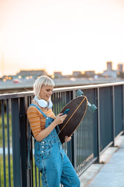 istock Young urban woman holding longboard and using smart phone 2164826770