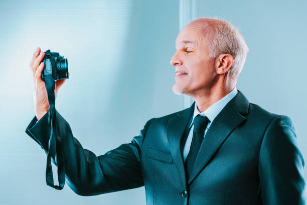 Confident businessman in suit with camera, capturing moment with smile. Blue background highlights modern photography concept. Ready to document memories with expertise and vision