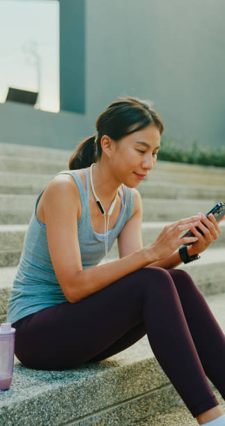 istock Young Asian female athlete runner drinking protein shake and using smartphone after exercise workout in urban park. Diet and healthy food workout exercise. Vertical Screen. 2164835533