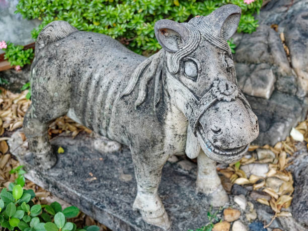 A rustic zebra statue in an old children's playground, showing signs of age with faded paint and surface wear. Positioned against a backdrop of green foliage and a wall adorned with hand-painted graffiti, the sculpture evokes a nostalgic charm.
