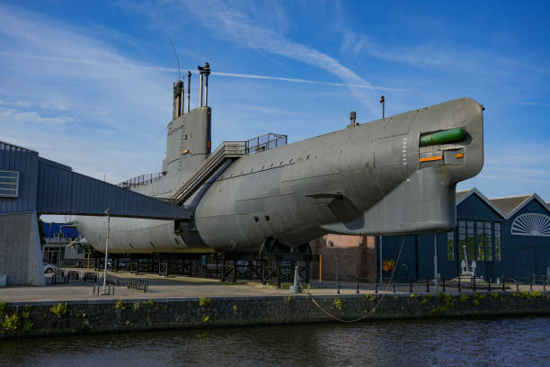 Callao, Peru. June 26,2025. A port scene features a black submarine converted into a museum, surrounded by several ships, docks, and the cloudy sky of a coastal day.