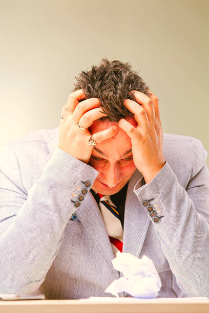 Businessman is suffering from a strong headache and feeling stressed while sitting at his desk with a crumpled piece of paper in front of him