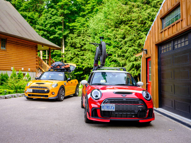 Tiny, Ontario, Canada- July 15, 2024. Two MINI COOPER cars on Muskoka cottgae vacation. Mid summer day. This is the third generation model F56 JCW, since BMW took over iconic brand of MINI. MINI featured in the photo is John Cooper Works model, the most powerful 2 door version. This compact car features engine build and designed by BMW, and packs even more power and torque than previous models, since 2002 to present. Original design clues and themes are still present on this brand new model. Mini has been around since 1959 and has been owned and issued by various car manufacturers.