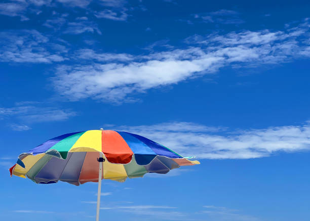 A brightly colored beach umbrella blowing in the wind against a deep blue sky in summer on vaction.