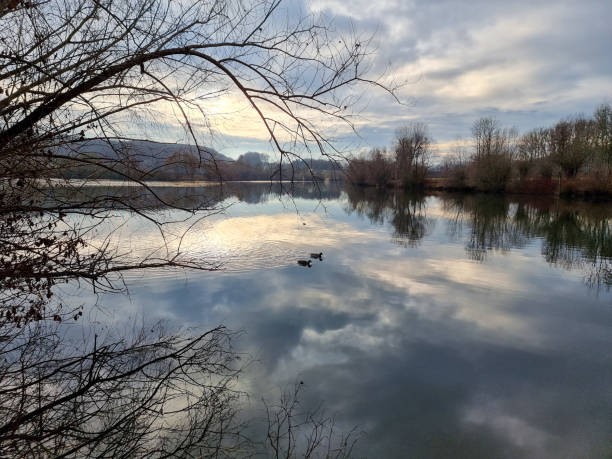 Beautiful idylic scene - sunset over the lake. Clouds lit by the setting sun are mirrored on the water surface. Around the lake trees grow.
