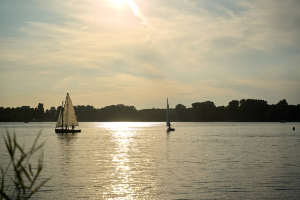 White sailboat lit by soft sunlight floating on the river against the cloudy sky before the storm.